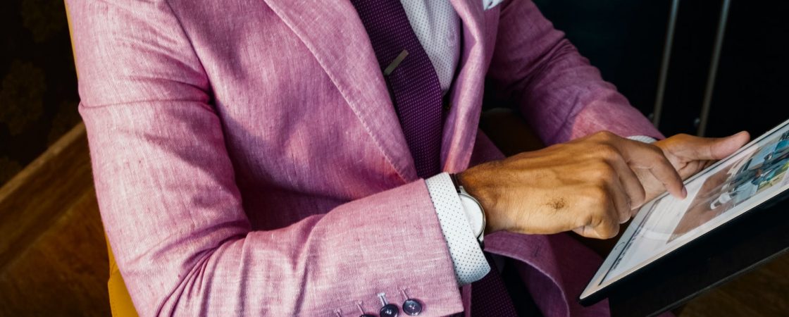 man wearing pink suit jacket holding using tablet computer