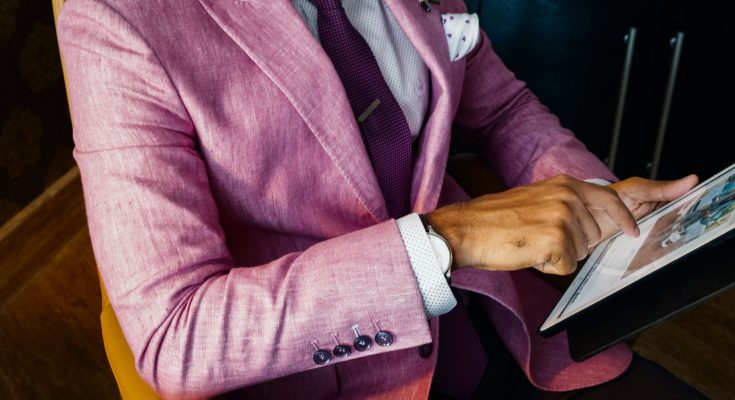 man wearing pink suit jacket holding using tablet computer