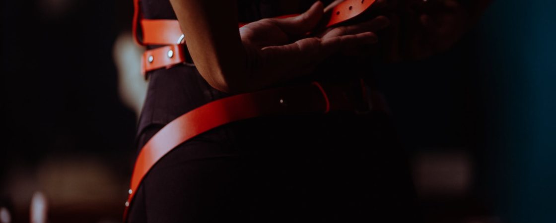 faceless woman fastening bdsm harness in dressing room